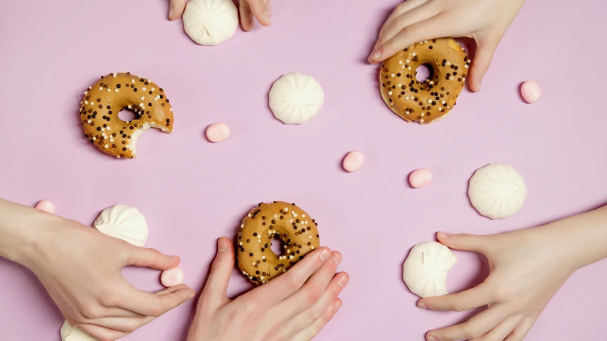 a group of people holding doughnuts on a pink surface, trending on pexels, pills, white and purple, four hands, animal - shaped bread