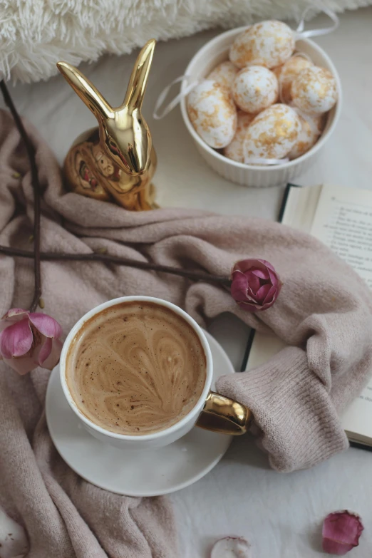 an open book sitting on top of a table next to a cup of coffee, a still life, by Lucia Peka, pexels contest winner, romanticism, easter, brown and gold color palette, latte art, bunny