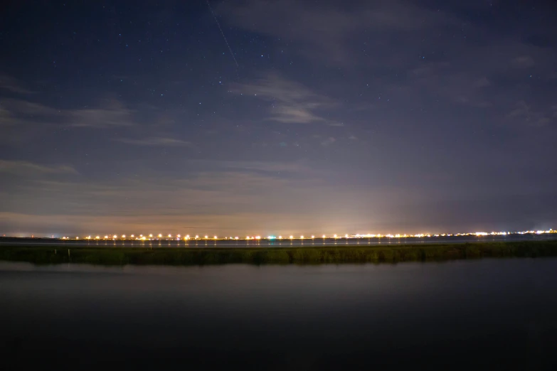 a large body of water under a night sky, a picture, by Adam Pijnacker, distant town lights, marsh, light trail, 2022 photograph