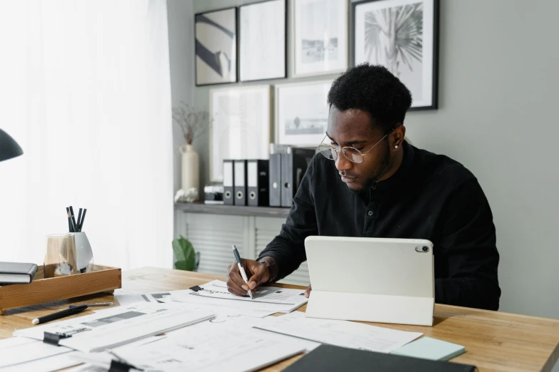 a man sitting at a desk working on a laptop, a drawing, by Carey Morris, pexels contest winner, african canadian, writing on a clipboard, low quality photo, thumbnail