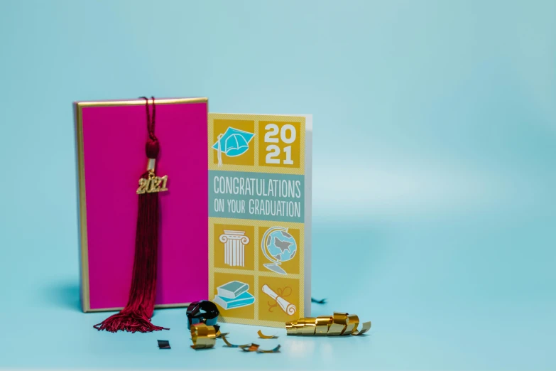 a book sitting on top of a table next to a book, tassels, gold encrustations, at college, pink and teal