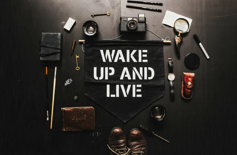 a black bag with wake up and live written on it, trending on pexels, still life photo of a backdrop, banner, symbols of live, flatlay