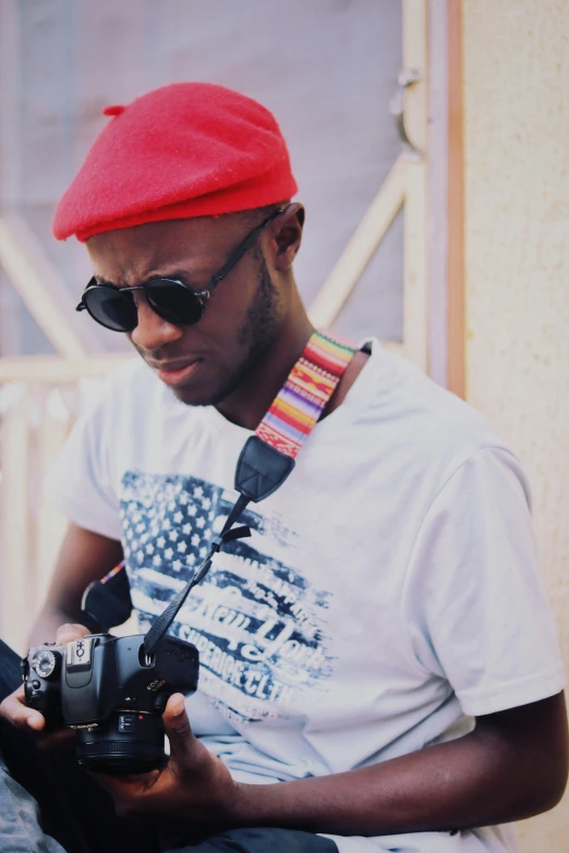 a man in a red hat is holding a camera, by Chinwe Chukwuogo-Roy, unsplash, photorealism, wearing sunglasses and a cap, low quality photo, colored, casually dressed