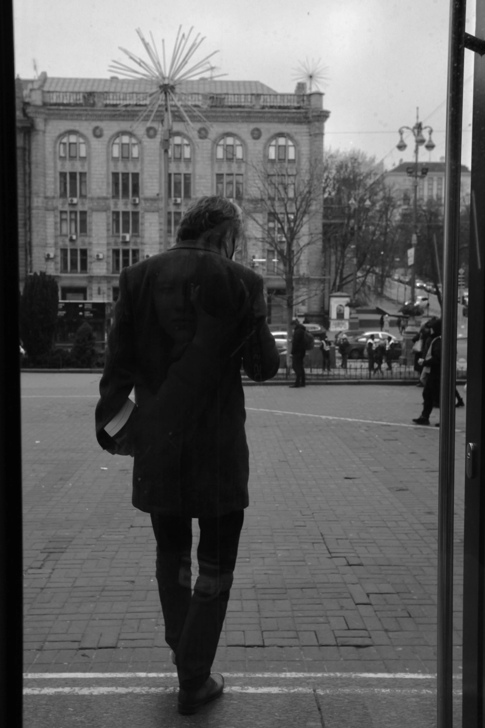 a black and white photo of a man walking down the street, a black and white photo, happening, lviv, \!cinestill 50d! film photo, about to enter doorframe, ( ( wearing a long coat ) )