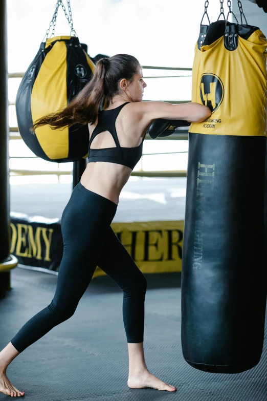 a woman standing next to a punching bag, happening, black and yellow, leggings, back arched, profile image