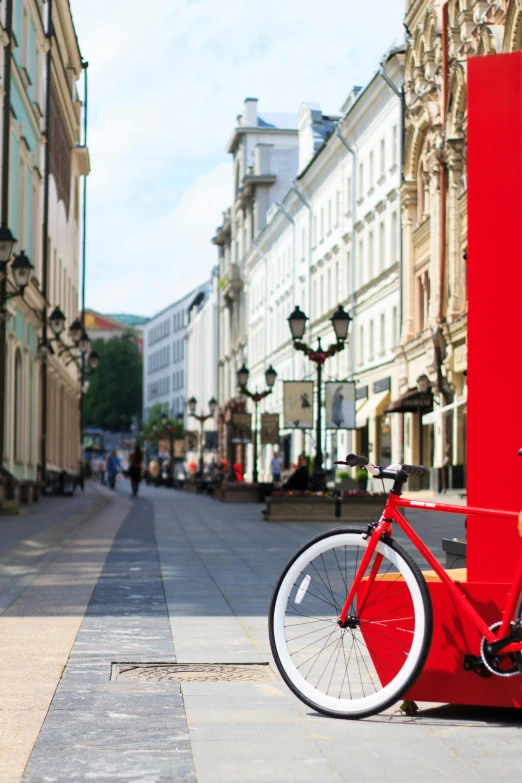 a red phone booth with a bicycle parked next to it, by karlkka, outdoors european cityscape, long street, demur