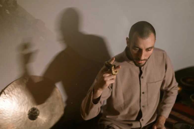 a man smoking a cigarette next to a drum, an album cover, inspired by Nadim Karam, pexels contest winner, antipodeans, holding a crystal ball, softly shadowed, press shot, holding a wood piece