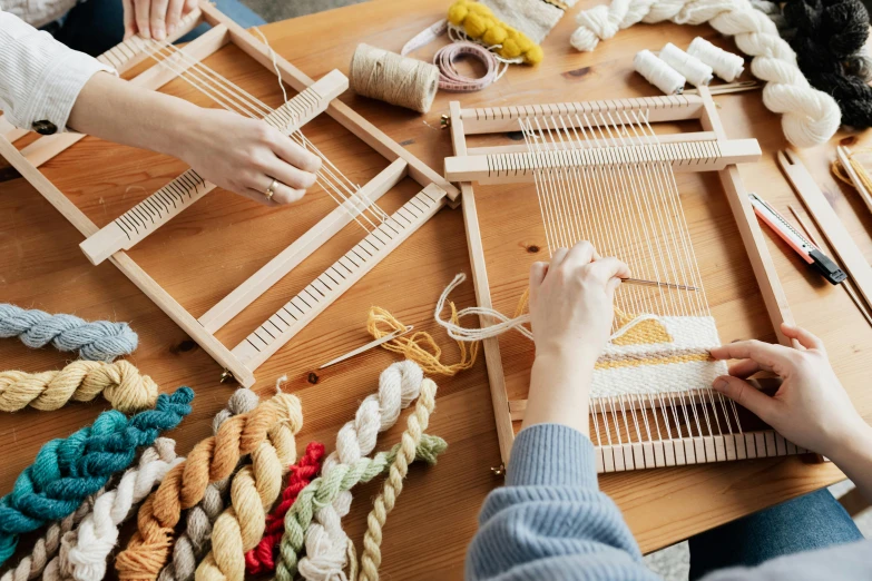 a woman sitting at a table working on a weaving loom, trending on pexels, arts and crafts movement, group photo, knolling, a wooden, on a canva