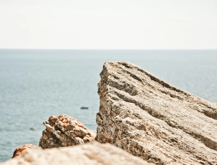 a man standing on top of a rock next to the ocean, by Rachel Reckitt, unsplash, close up shot a rugged, rock texture, on a canva, croatian coastline