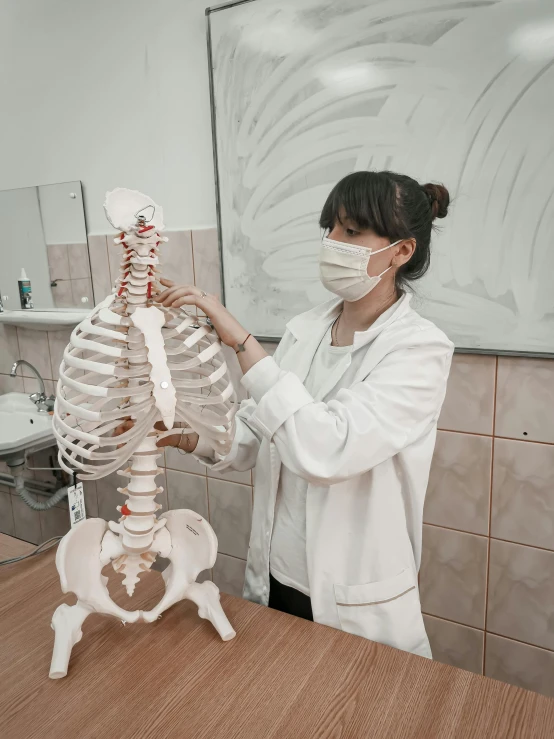 a woman in a white lab coat holding a model of a human skeleton, pexels contest winner, academic art, gif, rib cage, asian female, instagram picture