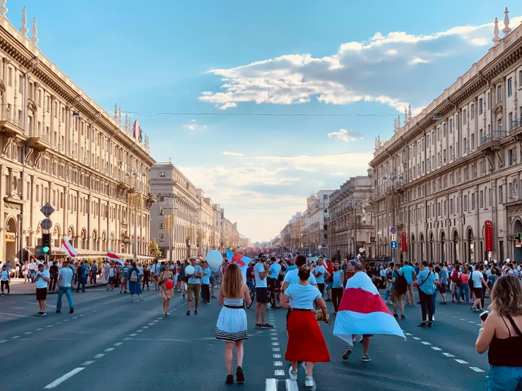 a crowd of people walking down a street next to tall buildings, by Julia Pishtar, pexels contest winner, socialist realism, president of belorussia, holding a white flag, italian, panoramic view of girl