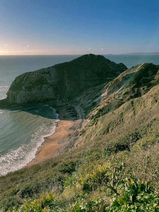 a large body of water sitting on top of a lush green hillside, by Colin Middleton, unsplash contest winner, chalk cliffs above, dramatic warm morning light, overlooking the beach, today\'s featured photograph 4k