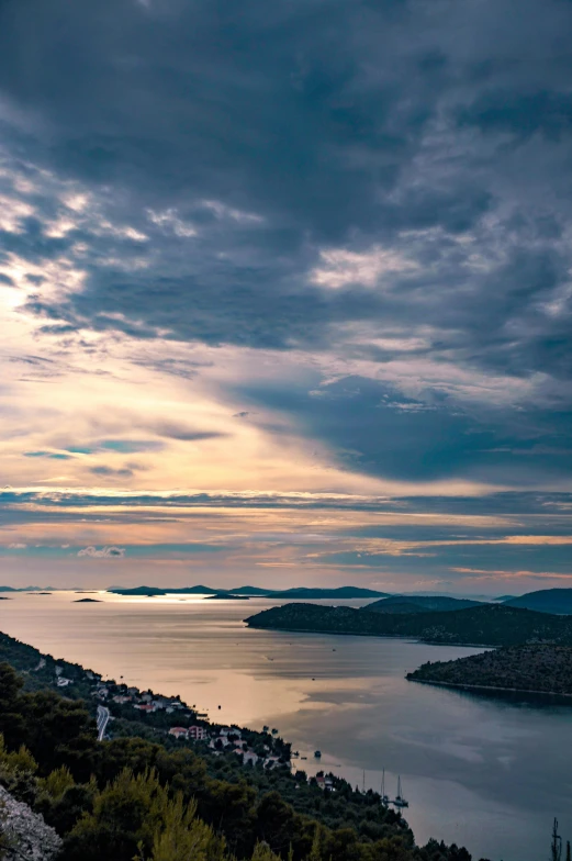 a large body of water sitting on top of a lush green hillside, by Daren Bader, unsplash contest winner, croatian coastline, hazy sunset with dramatic clouds, islands, urban surroundings