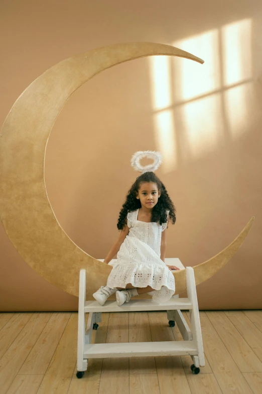 a little girl sitting on top of a wooden chair, inspired by Ida Rentoul Outhwaite, pexels contest winner, light and space, angel halo, imaan hammam, on moon, white crown