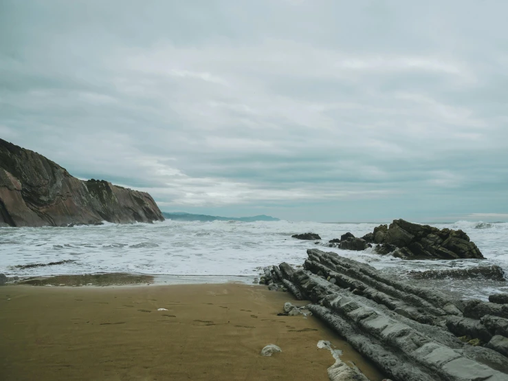 a large body of water sitting on top of a sandy beach, inspired by Thomas Struth, unsplash, romanticism, overcast gray skies, cliffs, a wooden, profile image