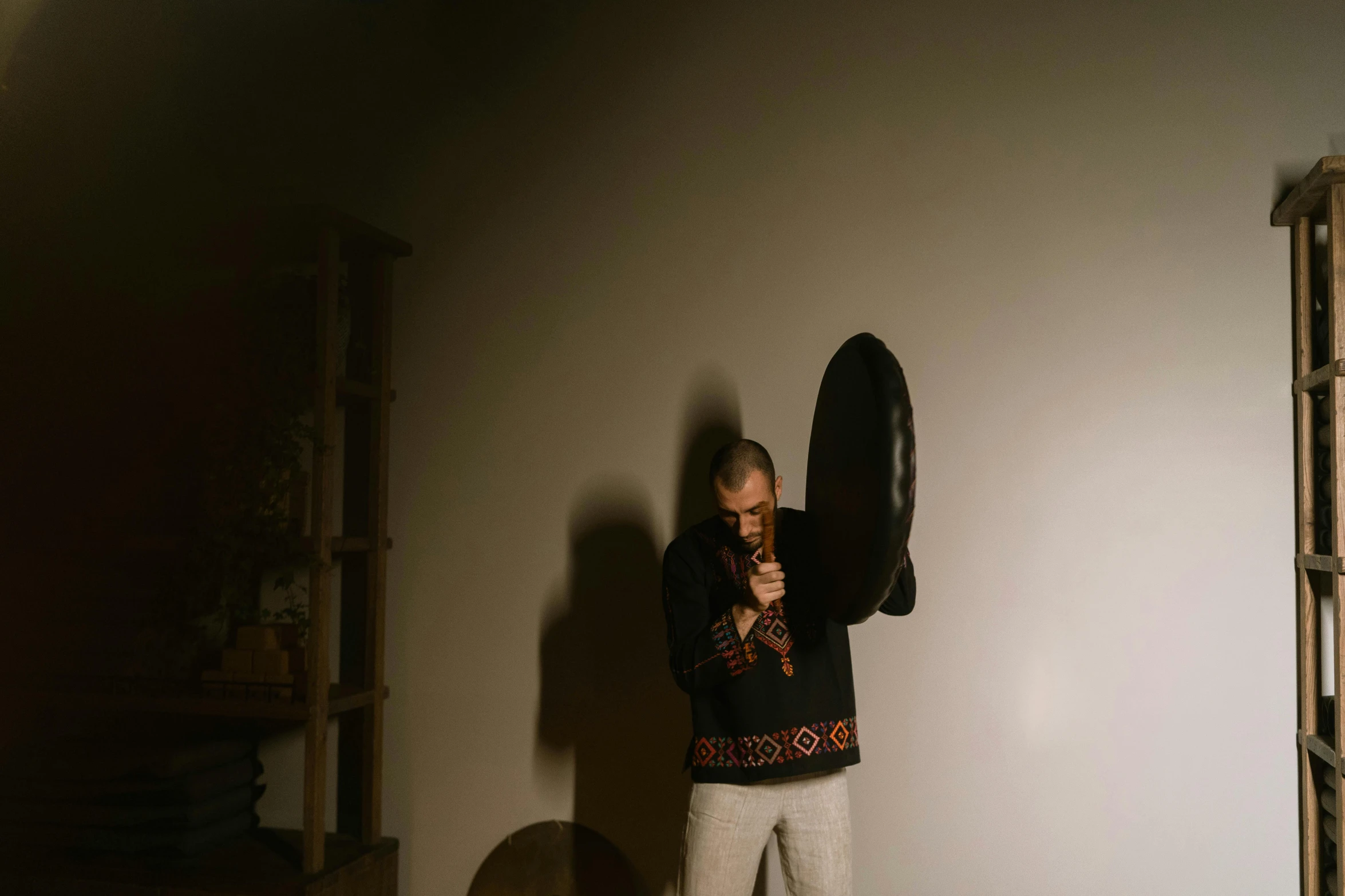 a man standing in a room with a hat on his head, an album cover, unsplash, hurufiyya, holding a shield, dramatic press photo, folklore, demna gvasalia