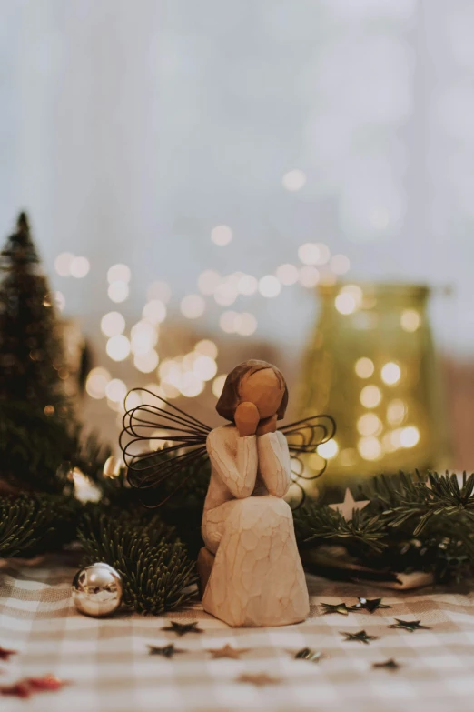 a couple of figurines sitting on top of a table, by Jessie Algie, pexels contest winner, fairy lights, angel in white linen, winter photograph, tree in the background