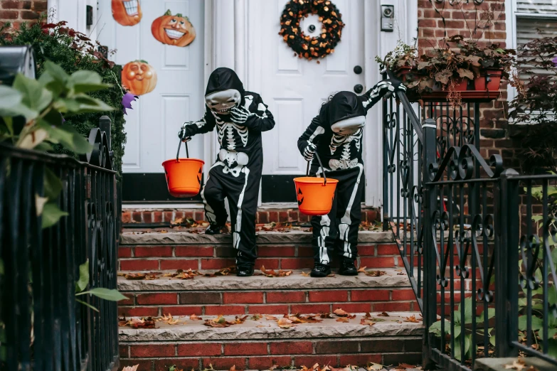 a couple of people sitting on the steps of a house, skeletons, trick or treat, unsplash photo contest winner, cute boys