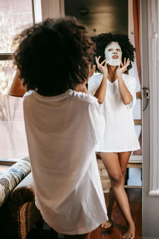 a woman that is standing in front of a mirror, happening, white mask, with afro, dressed in a white t shirt, wearing a nightgown