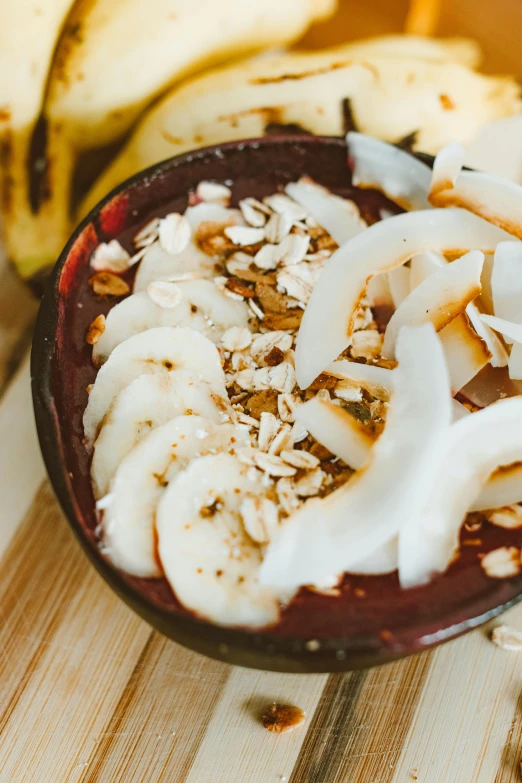 a close up of a bowl of food with bananas in the background, by Daniel Lieske, trending on unsplash, maroon, yogurt, coconuts, made of glazed