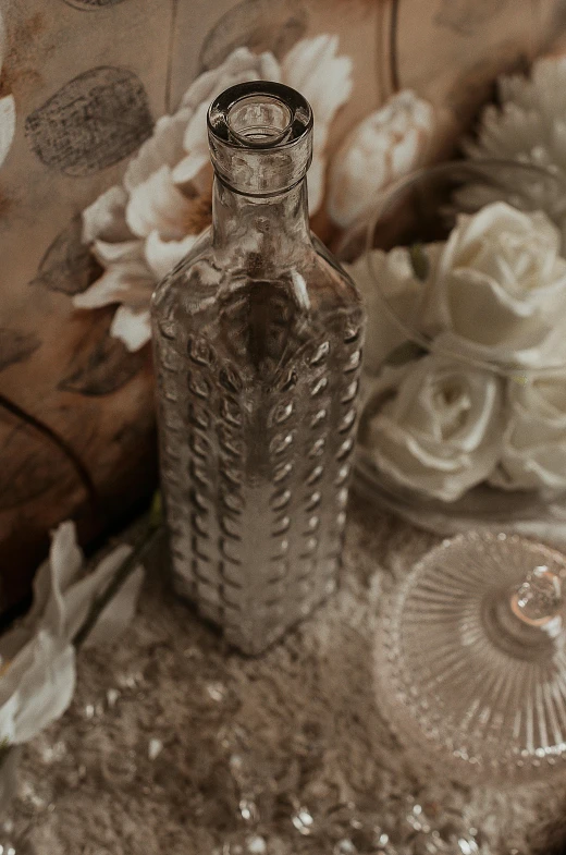 a glass bottle sitting on top of a table, a still life, inspired by Lionel Lindsay, unsplash, renaissance, exquisite floral details, soft sepia tones, potions, patterned