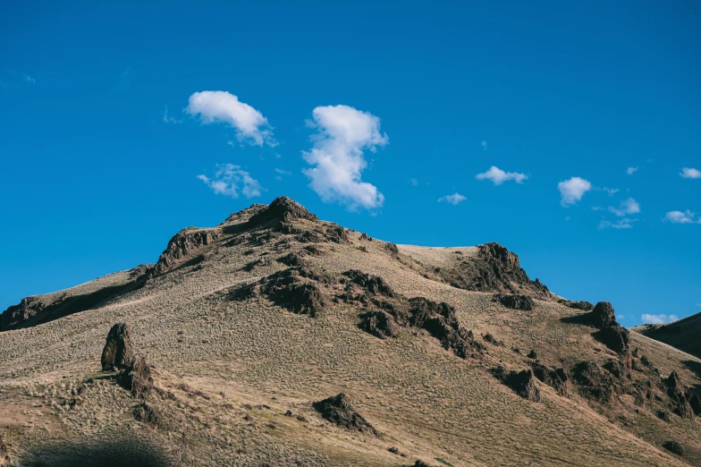 a man riding a motorcycle down a dirt road, unsplash, les nabis, light blue sky with clouds, in the distance is a rocky hill, photo of genghis khan, “ aerial view of a mountain