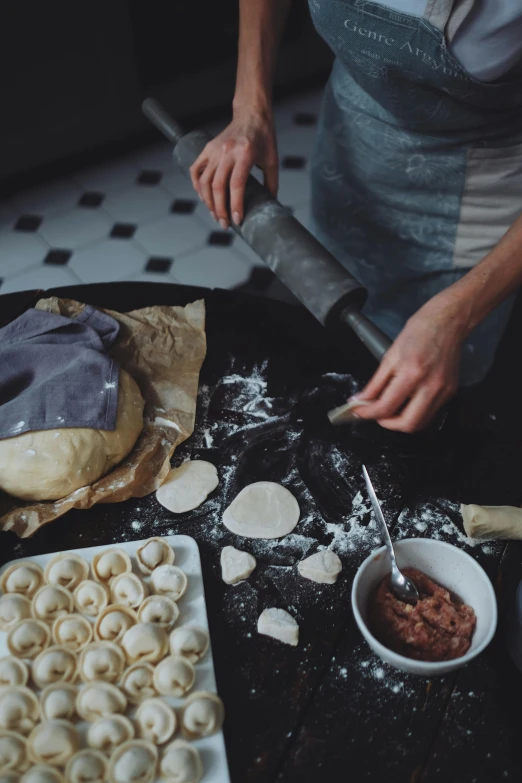 a woman in an apron preparing food on a table, a still life, pexels contest winner, crispy buns, dramatic details, winter, college