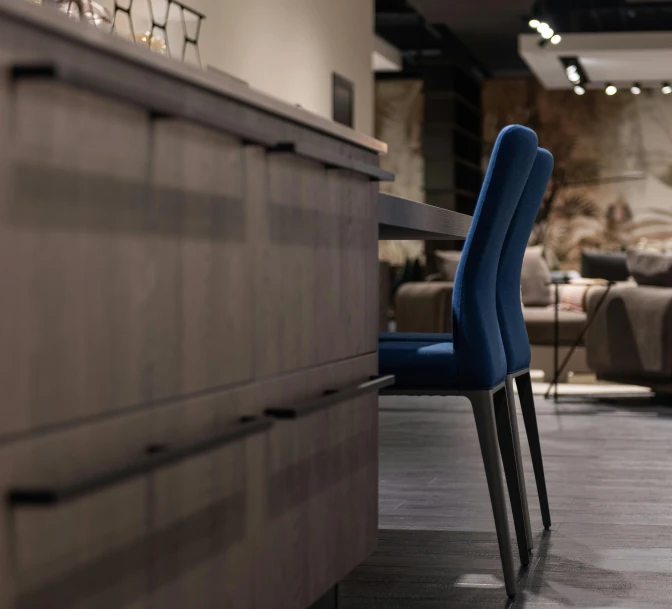 a blue chair sitting on top of a wooden table, by Raphaël Collin, pexels contest winner, luxury bespoke kitchen design, show room scene, calmly conversing 8k, posed in profile