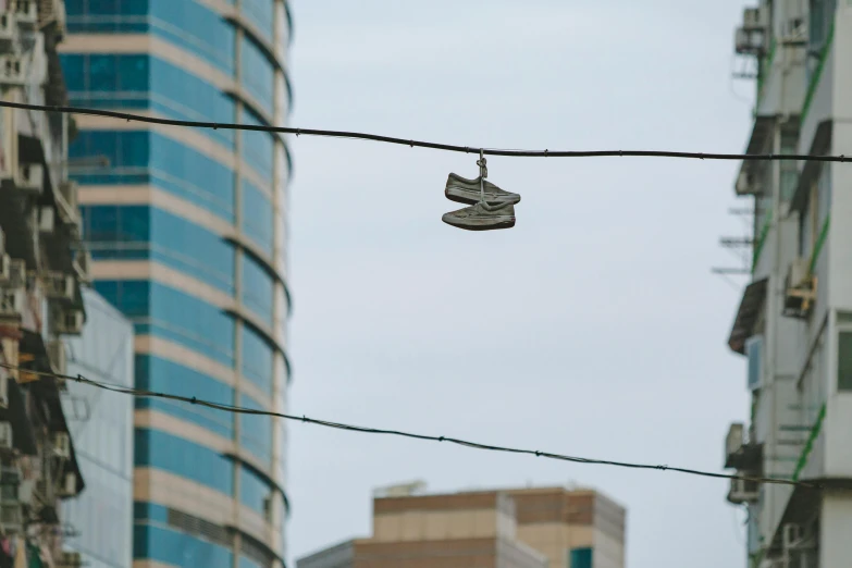 a pair of shoes hanging from a wire in a city, by Dan Frazier, unsplash, ap, slight overcast, high quality photo, ap press photo