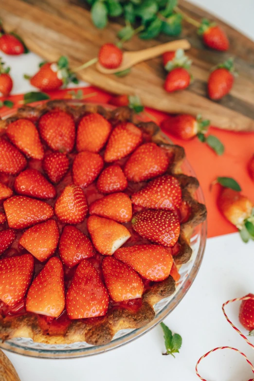 a table topped with a pie covered in strawberries, coral red, product shot, fruit, bottom body close up