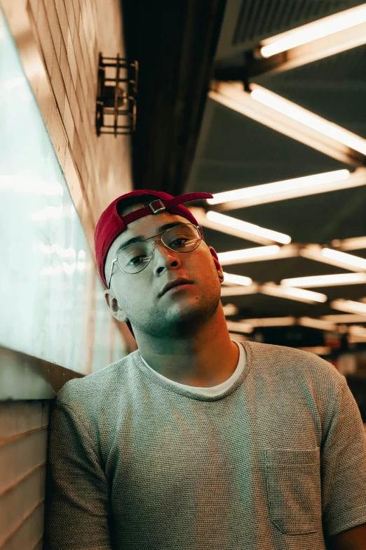 a man wearing a hat and glasses leaning against a wall, an album cover, by Robbie Trevino, pexels contest winner, wearing a red backwards cap, portrait soft low light, asher duran, shaven