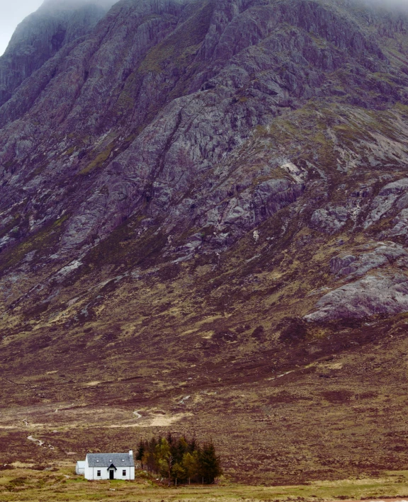 a house in the middle of a field with a mountain in the background, by Andrew Allan, pexels contest winner, in between a gorge, whealan, panoramic, dusty rock in background