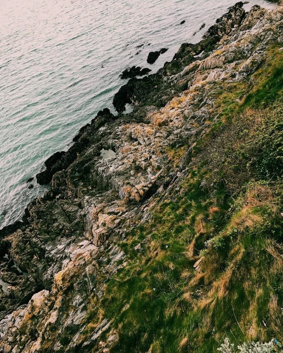 a man standing on top of a cliff next to the ocean, inspired by Elsa Bleda, pexels contest winner, grassy stones, high view, ((rocks)), calmly conversing 8k