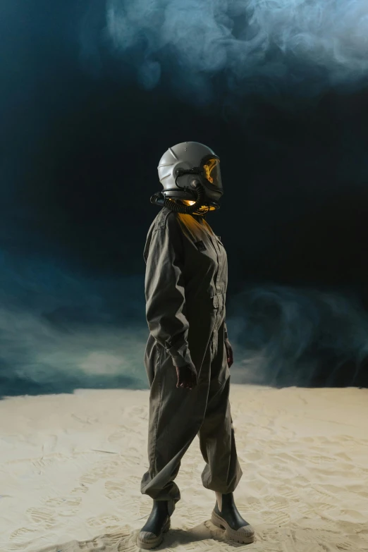a person standing in the sand with a helmet on, inspired by ridley scott, wearing flight suit, night sky, production photo, uniform off - white sky