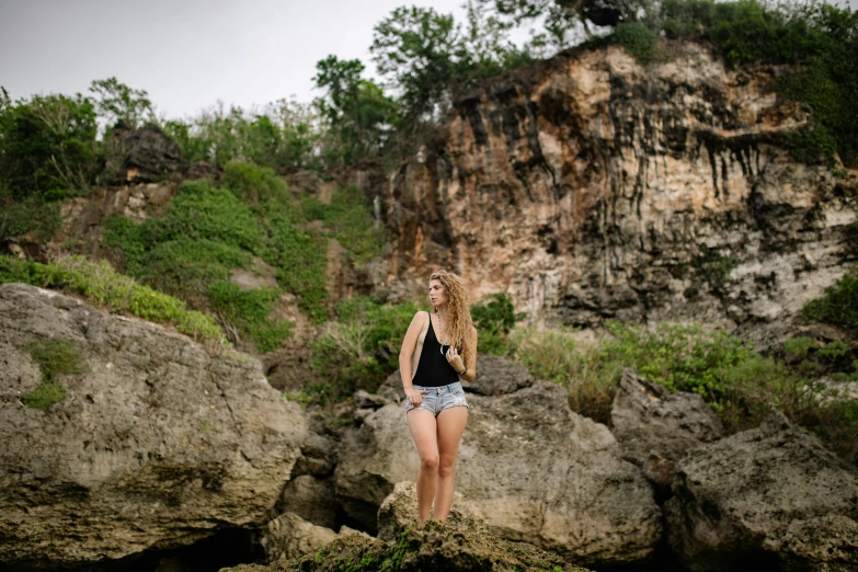 a beautiful young woman standing on top of a rock, a portrait, by Ella Guru, unsplash, wearing a camisole and shorts, avatar image, bali, half - length photo