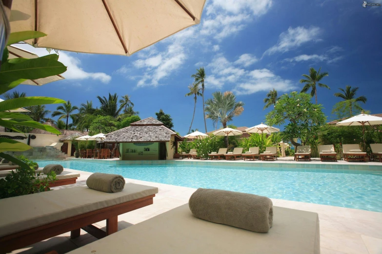 a couple of lounge chairs sitting next to a swimming pool, coconut trees, umbrellas, big sky, exterior shot