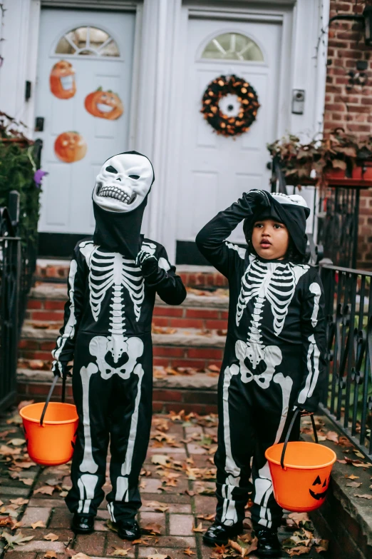 two children in skeleton costumes standing in front of a house, by Ellen Gallagher, pexels contest winner, snacks, brooklyn, black, small