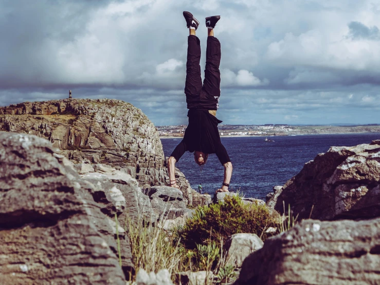 a man doing a handstand in front of a body of water, on a cliff, whealan, flying rocky island, doing a sassy pose