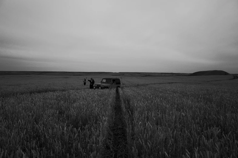 a black and white photo of a truck in a field, by Aleksander Kobzdej, unsplash, land art, people walking around, azamat khairov, new album cover, late evening
