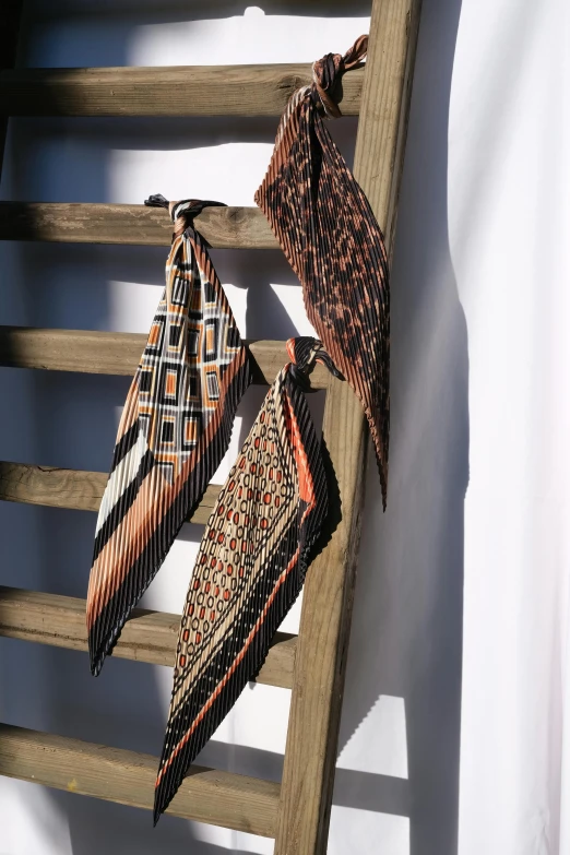 three ties hanging on a wooden ladder, by Nina Hamnett, unsplash, renaissance, orange and black tones, patterned scarf, detailed product shot, square