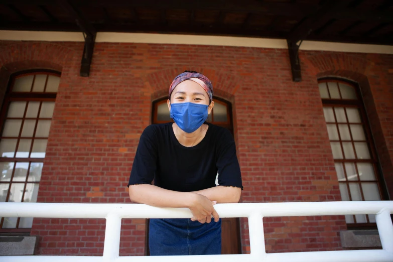 a woman wearing a face mask in front of a brick building, yan morala, post graduate, standing on rooftop, looking straight to camera