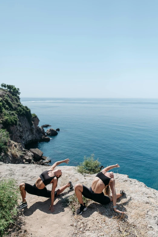 a group of people standing on top of a cliff next to the ocean, arabesque, doing splits and stretching, black sea, lush surroundings, flatlay