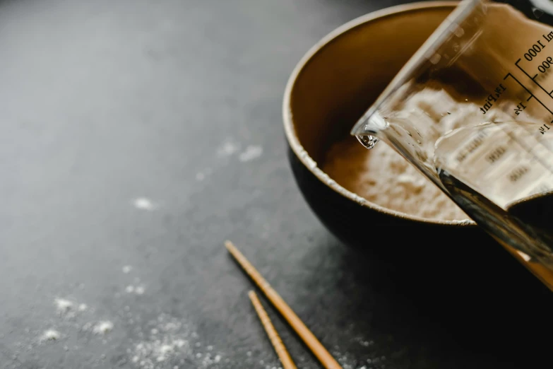 a close up of a bowl of food with chopsticks, a still life, unsplash, process art, background image, yeast, glassware, mortar and pestle