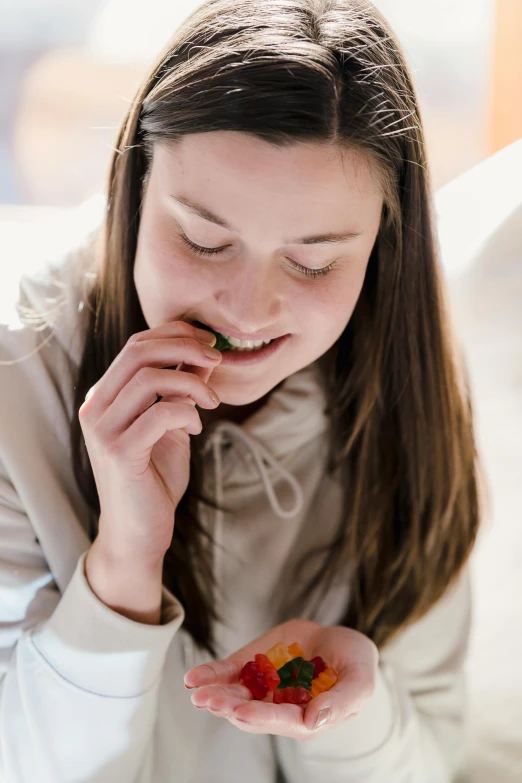 a woman sitting on a couch eating a piece of fruit, girl with brown hair, girl wearing hoodie, zoomed in, orange