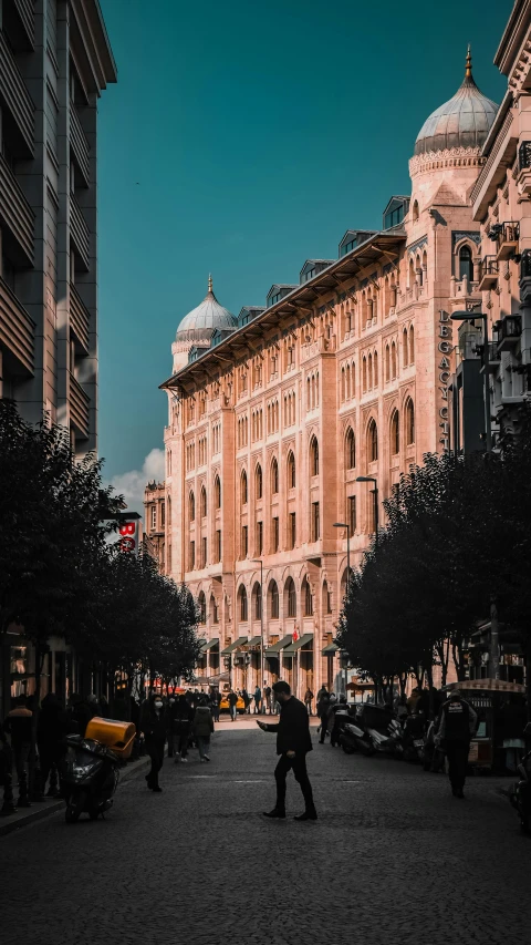 a man walking down a street next to tall buildings, by Ahmed Yacoubi, pexels contest winner, neoclassicism, assyrian, busy streets filled with people, pink marble building, square