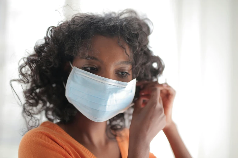 a woman in an orange shirt is wearing a face mask, pexels, hurufiyya, photo of a black woman, surgical supplies, with grey skin, curls