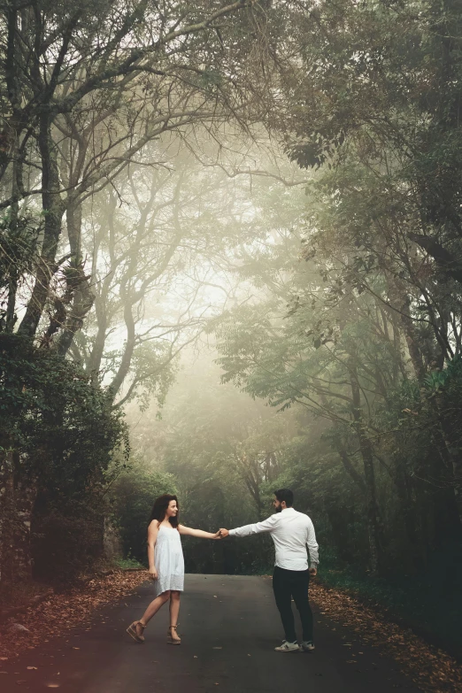 a man and woman holding hands in the middle of a road, a picture, by Lucia Peka, romanticism, placed in a lush forest, te pae, kahikatea, foggy