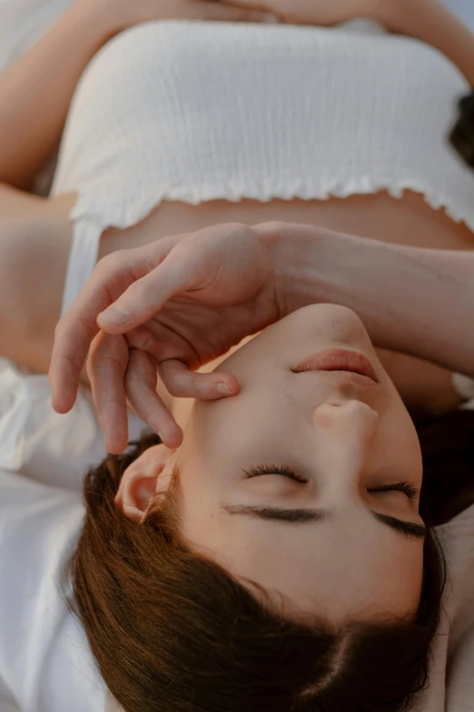 a woman laying on a bed with her eyes closed, inspired by Elsa Bleda, trending on pexels, aestheticism, square facial structure, greeting hand on head, high angle close up shot, pale skin