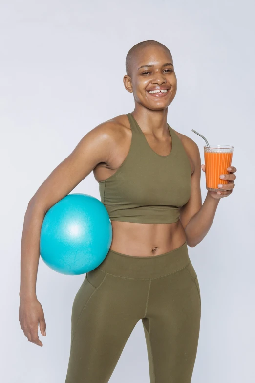 a woman in a sports bra top holding a drink and a ball, by Matija Jama, wearing an orange jumpsuit, dark skin tone, bald lines, moringa juice