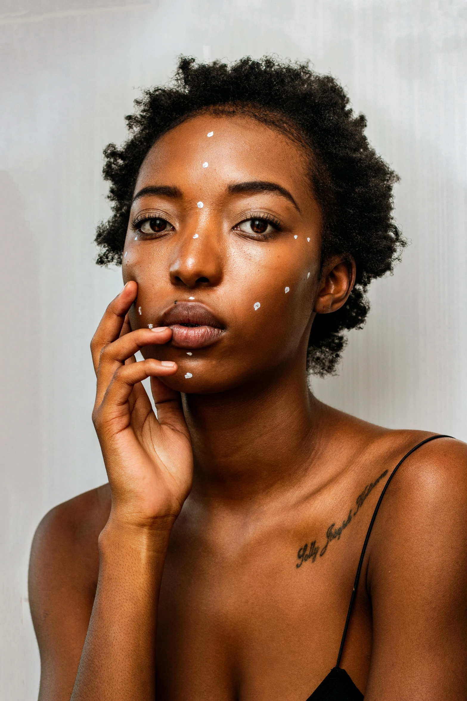 a woman with a lot of makeup on her face, by Lily Delissa Joseph, trending on pexels, afrofuturism, partially cupping her hands, white freckles, photoshoot for skincare brand, drawn with dots